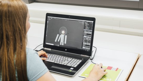 Mädchen mit langen Haaren sitzt vor Bildschirmund arbeitet mit 3D Design Blender