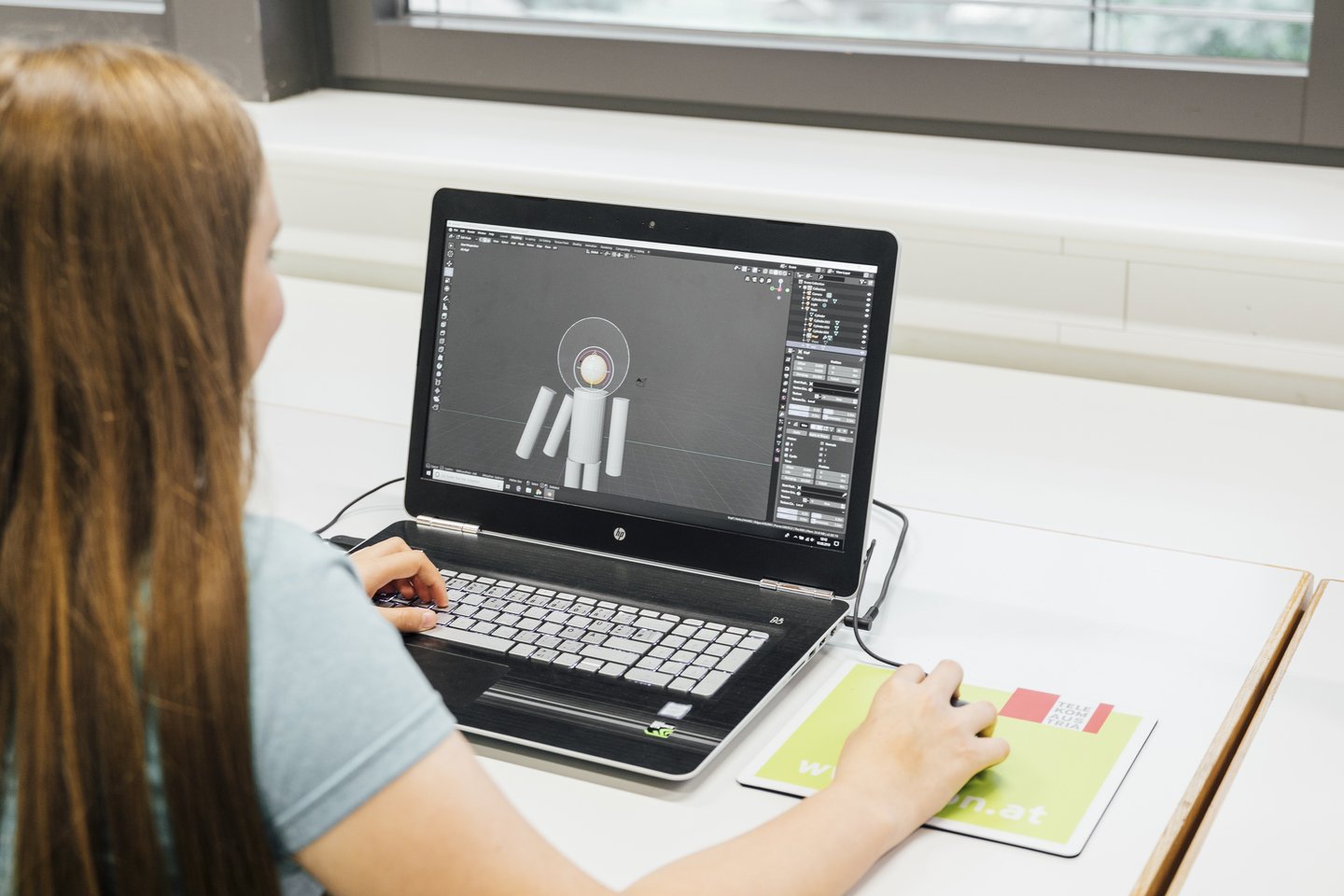 Mädchen mit langen Haaren sitzt vor Bildschirmund arbeitet mit 3D Design Blender